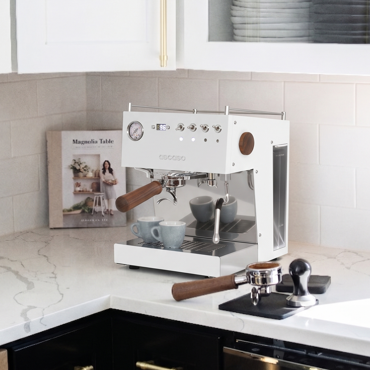 Espresso machine on a kitchen counter with a magazine and coffee cups nearby.